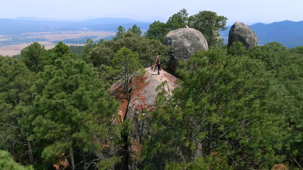 Woman ziplining from large granite rock above pine forest in Los Frailes, Tapalpa, with mountains in background