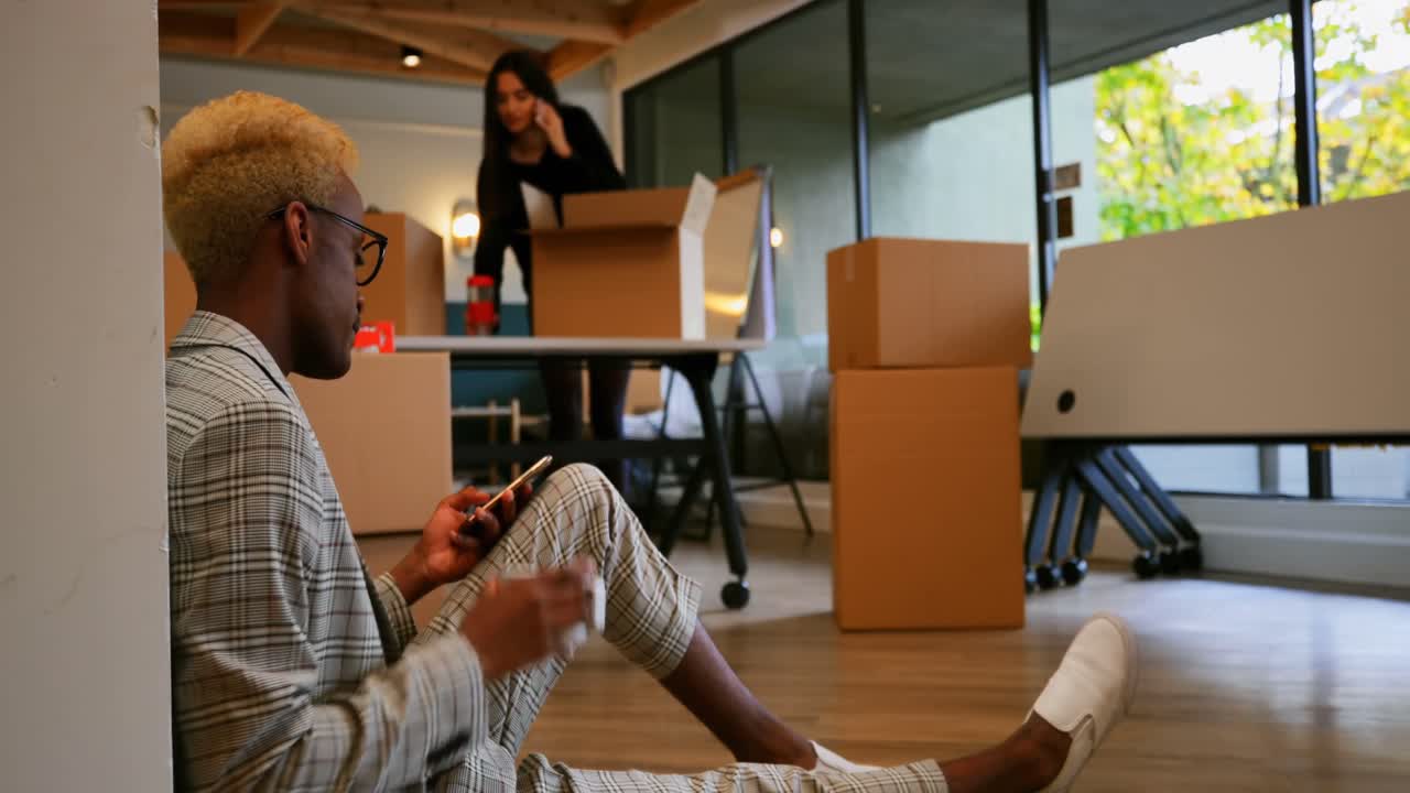 Side view of young black businessman using mobile phone and drinking coffee in modern office 4k