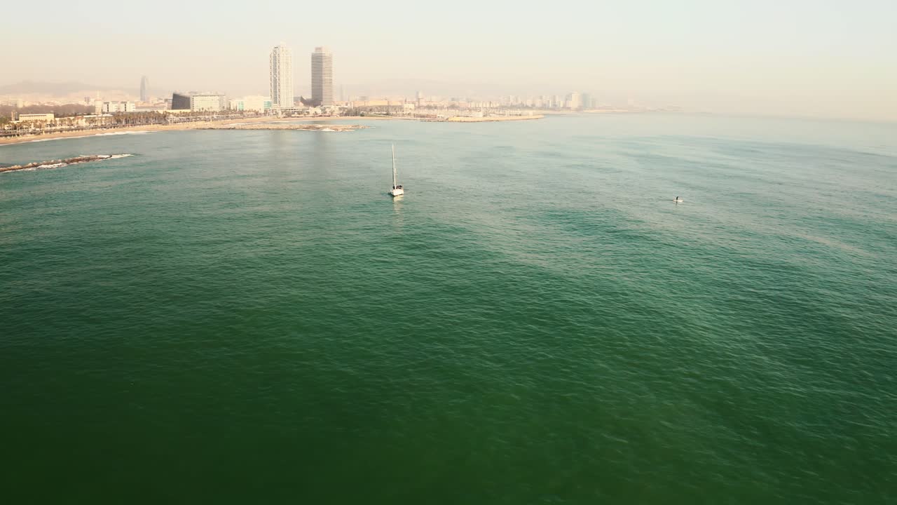 AERIAL: Parallax shot of a sailboat lying in the water off the coast of Barcelona, Spain