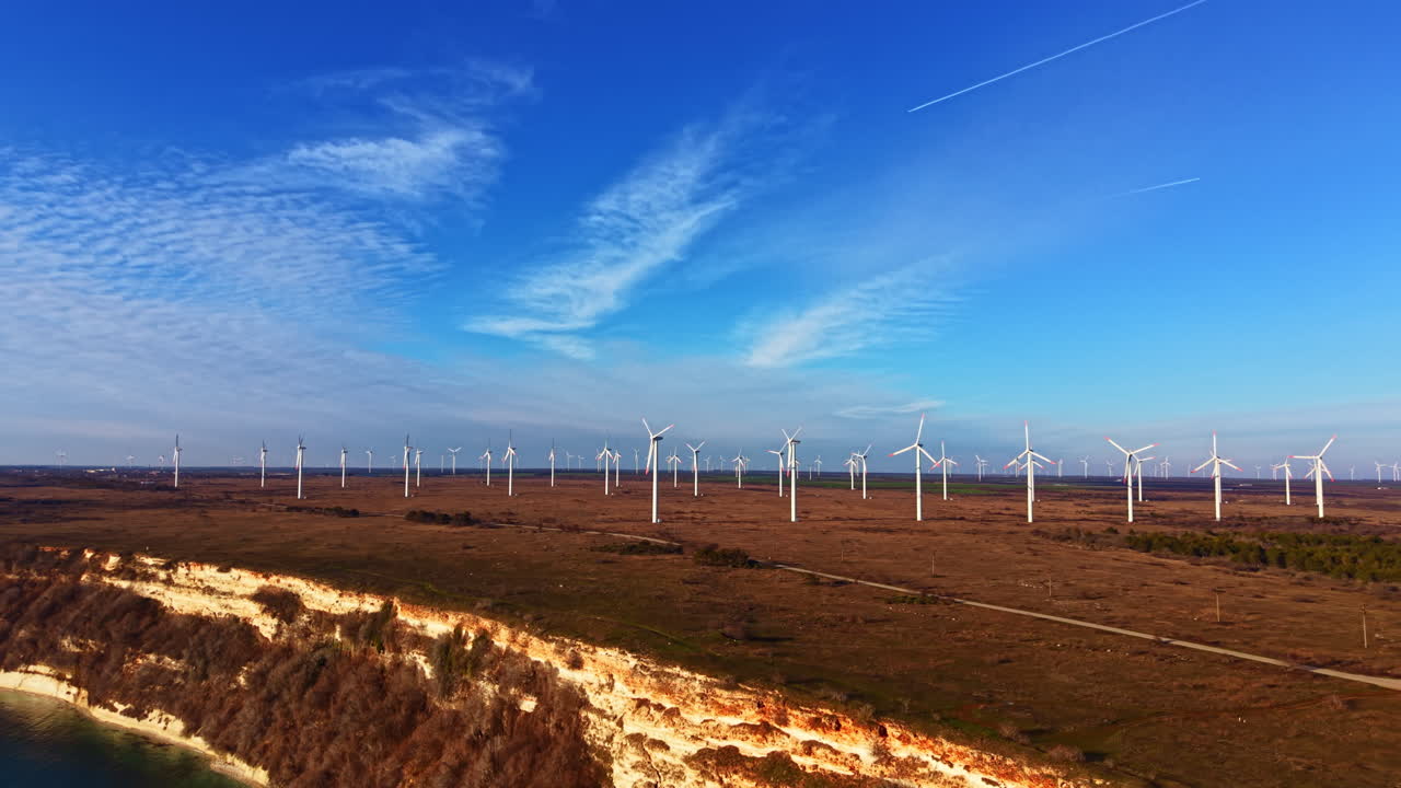 Turbinas eólicas em uma planície sob um céu azul com nuvens brancas e um horizonte distante mostrando uma paisagem natural em um dia ensolarado