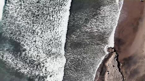 Birds-eye-view-flying-over-the-surfers-and-beach-at-Piha-Beach-in-Auckland-New-Zealand