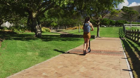 mujer afroamericana con mochila montando un scooter en el parque