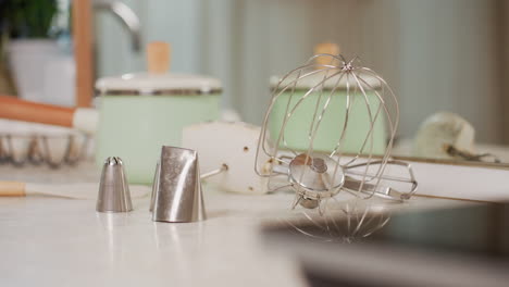 close up of modern kitchen corner with silver blender machine, chrome tap, ceramic containers, decorative oil dispenser, potted plants, and vintage glass lamp on windowsill