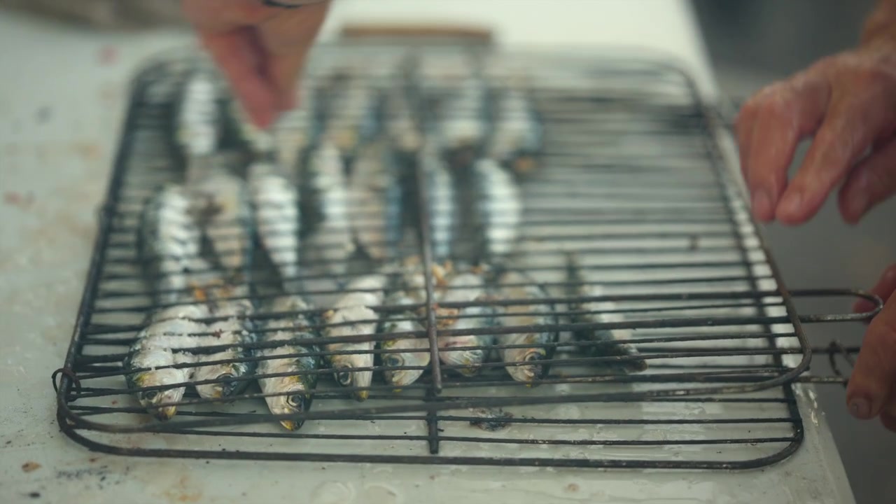 Person's hands preparing small fish for grilling on a bbq. Cooking fresh seafood outdoors for a healthy meal