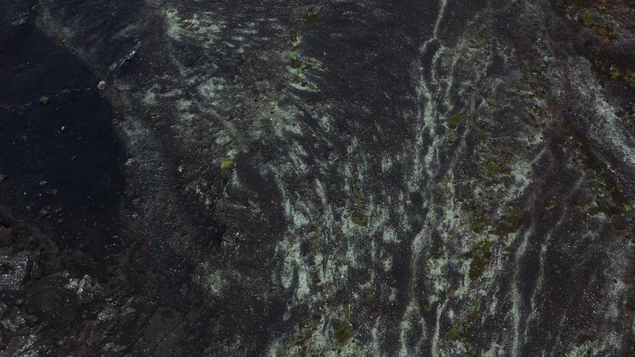 Top-down drone glides over Iceland black lava rock revealing white mineral patterns.