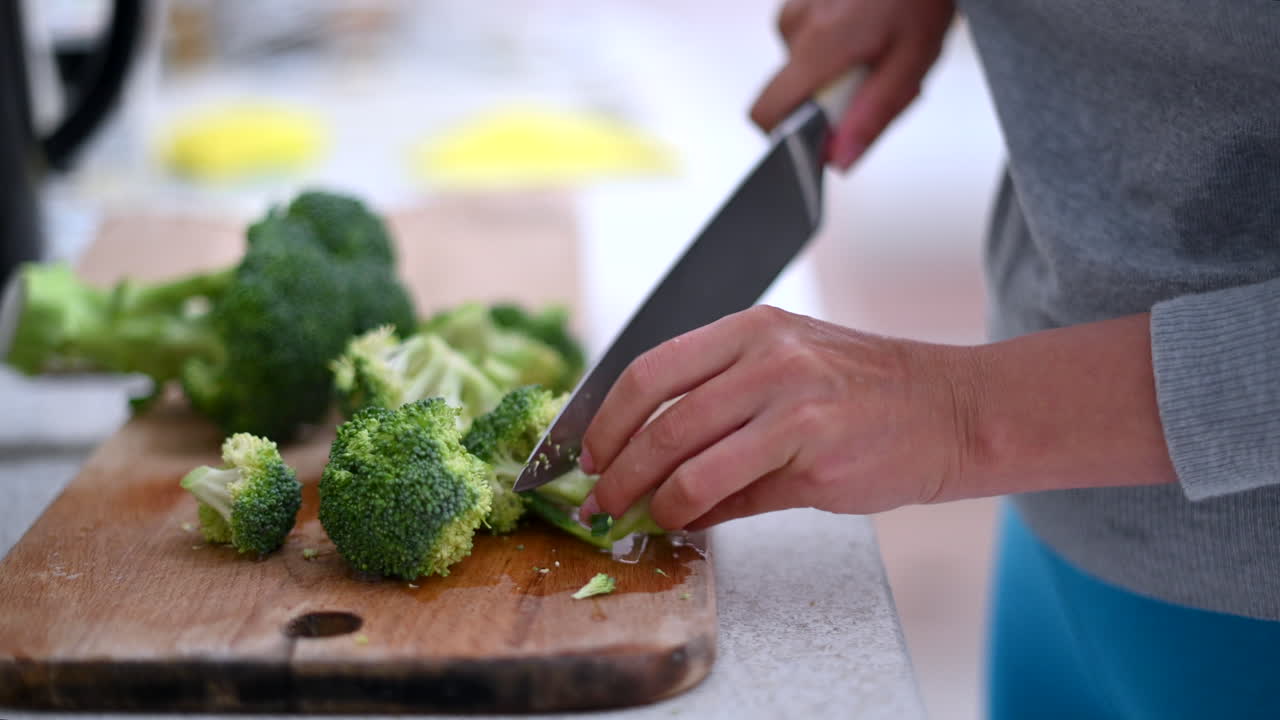 Woman cutting green broccoli at the kitchen