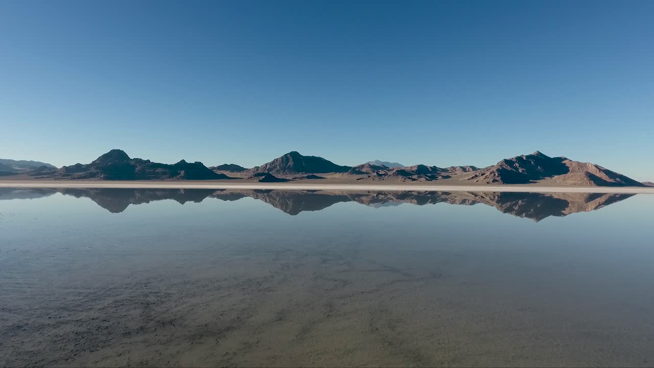 una toma aérea de drones revela agua tranquila que cubre las salinas de bonneville y refleja las montañas escarpadas distantes