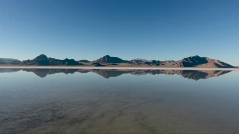 An-aerial-drone-shot-reveals-smooth-water-covering-the-Bonneville-Salt-Flats-and-reflects-the-distant-craggy-mountains