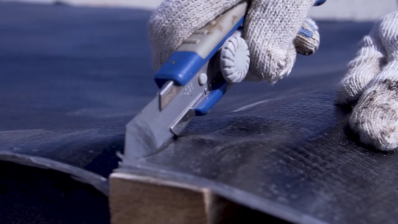 Person cutting a roofing material with utility knife