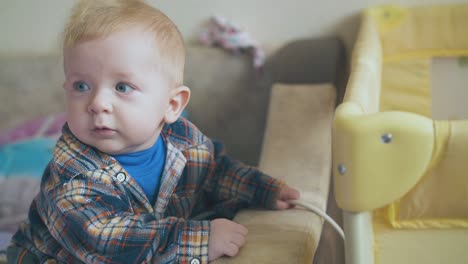 cute boy in shirt plays with cable standing at playpen