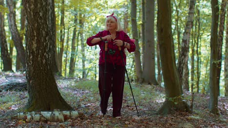 Senior-elderly-tourist-grandmother-training-Nordic-walking-with-ski-trekking-poles,-hiking-in-wood