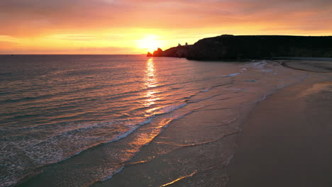 linear side aerial of sun setting over waves at empty beach