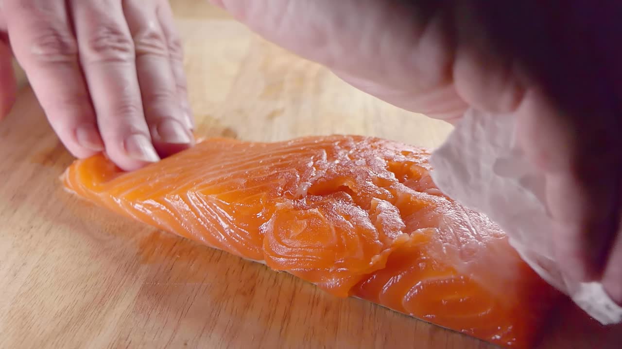 Close Slow Motion Shot of Patting a Salmon Fillet Dry With Paper Towels Prior to Cooking in the Kitchen