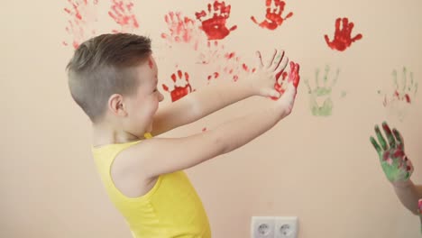 madre joven con su pequeño hijo están mezclando colores en sus manos usted deja hermosas huellas de manos en la pared. madre e hijo