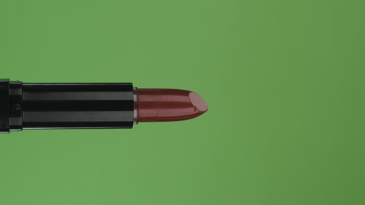 rotación horizontal de un lápiz labial rojo abierto, en una pantalla verde. primer plano.