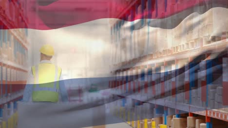 Animation-of-waving-netherlands-flag-against-caucasian-male-worker-checking-stock-at-warehouse