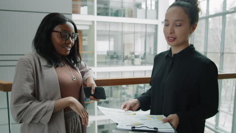 multiethnic female colleagues discussing business papers