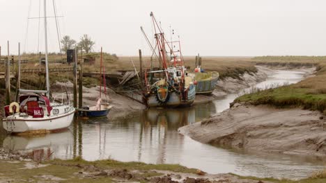 Yachts-and-fishing-boat-moored-on-Steeping-River-at-Gibraltar-Point,-with-the-tide-out-showing-mud-banks