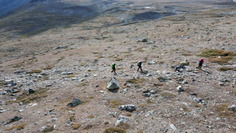 people-hiking-mountain-valley,-backpack-summit-trail,-walking-through-mountain-plateau,-drone-Birdseye-perspective-overview,-shot-tilt-up-to-horizon,-aerial