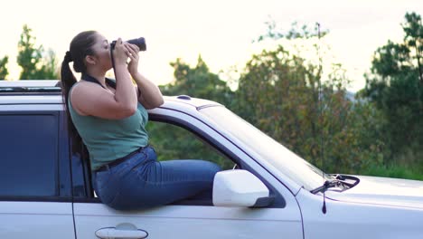 photographer woman sitting in the window of her 4x4 offroad suv car with a camera in her hands, taking a photograph