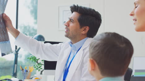 médico en bata blanca con madre e hijo en la oficina mirando imágenes de resonancia magnética o tomografía computarizada