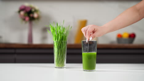 placing a straw into a vibrant green wheatgrass juice on a modern kitchen counter