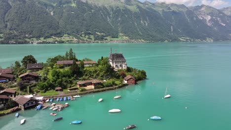 drone pushes forward, iseltwald village surrounded by lake water, parked boats and stunning green mountains at lake brienz, switzerland