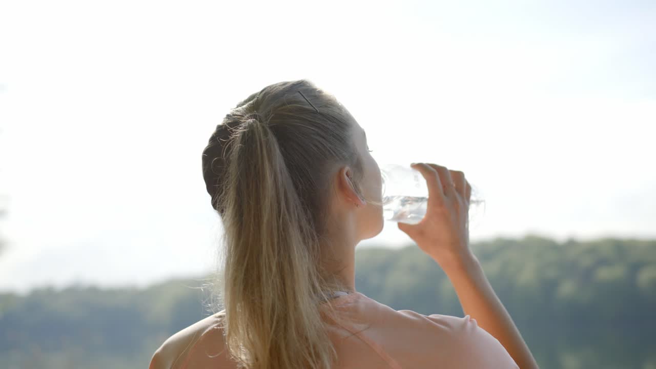 Donna che beve acqua da una bottiglia davanti a un lago.