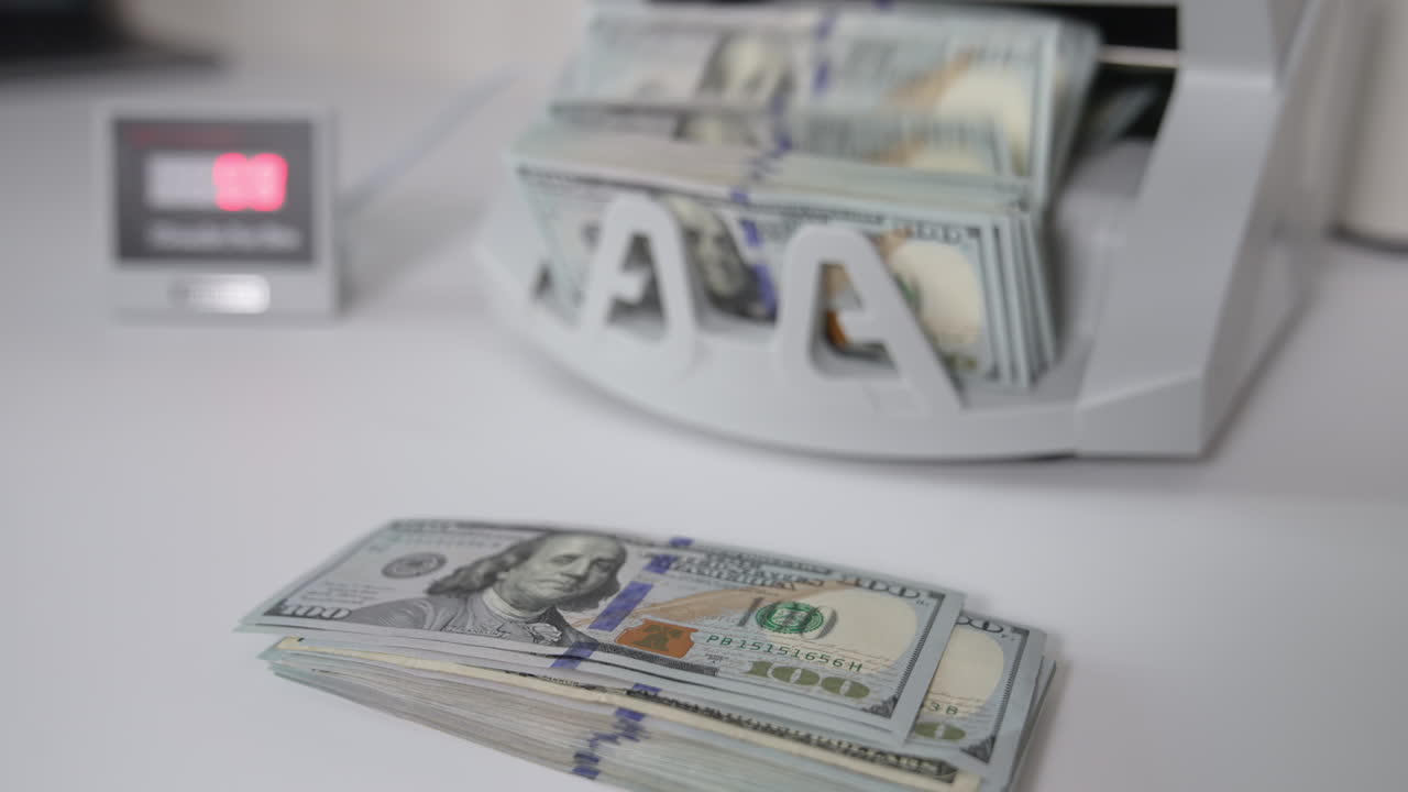 A wad of USD dollars is on the table. One hundred dollar bills are counted in the money machine. Blurred background.