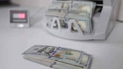 a wad of usd dollars is on the table. one hundred dollar bills are counted in the money machine. blurred background.