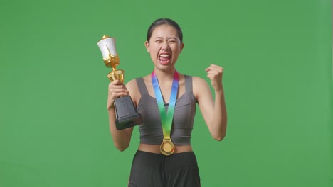 asian woman with a gold medal and trophy screaming goal celebrating winning as the first winner on green screen background in the studio