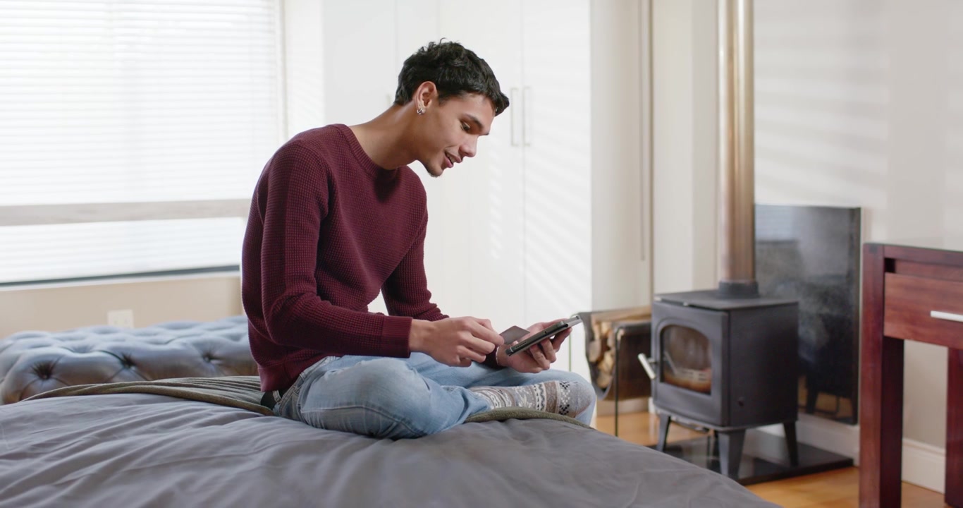 African American man in maroon sweater tapping tablet on bed, picking up card, tapping for payment