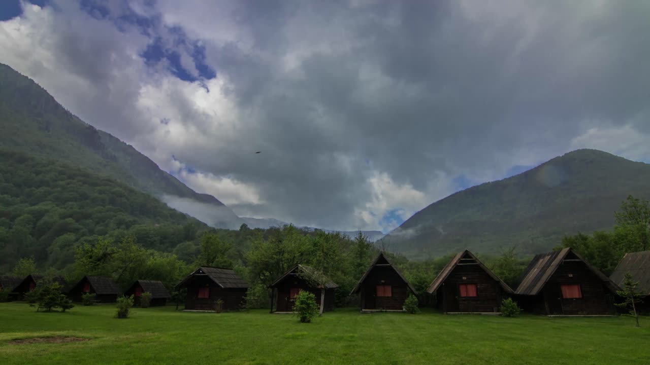 Experience the rustic charm of Kamp Ivona Tara, nestled amidst majestic mountains. Traditional wooden cabins offer a peaceful retreat in this stunning natural landscape, under a dramatic sky.