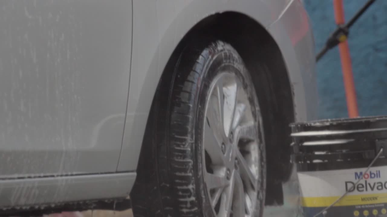 Close up person washing car with a hose with pressurized water. Slow motion
