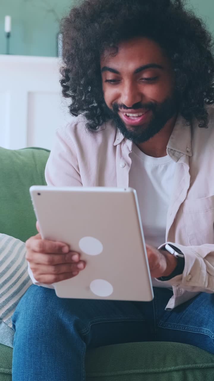 Young enthusiastic arabian man freelancer uses tablet computer sits on sofa