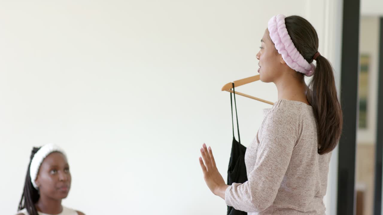 Amiche afroamericane a casa, una donna tiene un vestito su una gruccia mentre l'amica le chiede consiglio