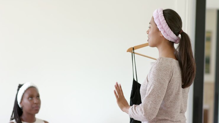 Amiche afroamericane a casa, una donna tiene un vestito su una gruccia mentre l'amica le chiede consiglio