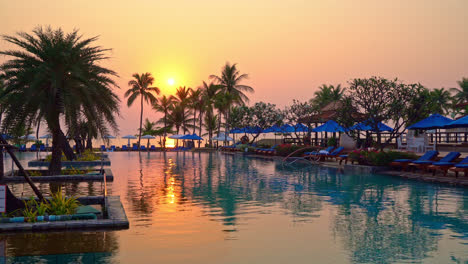 Piscina-De-Cama-Y-Sombrilla-Alrededor-De-La-Piscina-Con-Cielo-De-Puesta-De-Sol-O-Amanecer