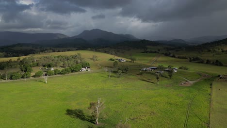 Aerial-views-over-farmland-in-Lamington-in-the-Scenic-Rim-with-rain-fall-in-the-distance,-Queensland,-Australia