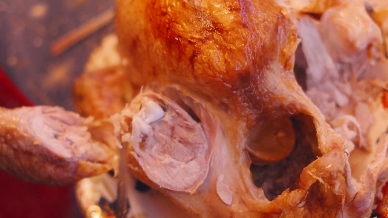 pierna de pavo asada siendo tallada de la articulación principal con un cuchillo afilado en la mesa de cena para navidad o cena de acción de gracias. sirviendo comida casera tradicional en xmas para celebrar 4k.