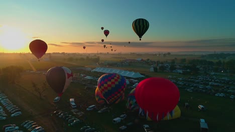 Vista-Aérea-De-Un-Festival-De-Globos-Aerostáticos-Temprano-En-La-Mañana-Despegue-Hacia-El-Sol-En-Un-Día-Soleado-De-Verano-En-El-Campo-De-Pensilvania