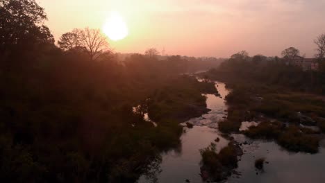 Drone-Moviéndose-Hacia-Adelante-Y-Hacia-Arriba-Hacia-Un-Sol-Naciente-Con-Un-Primer-Plano-De-Río