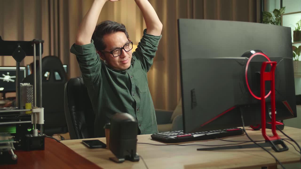 Asian Man Stretching While Works On Personal Computer And 3D Printer In Home Office, He Works At Night