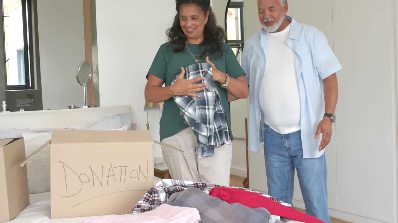 Casal afro-americano vendo caixas de doação, dobrando e colocando camisas xadrez na cama para caridade.