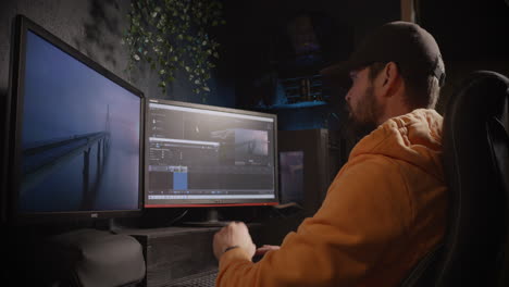 Male-video-editor-wearing-a-black-cap,-looking-into-desktop-monitors-during-post-processing-work