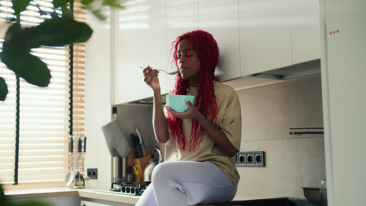 mujer de cabeza roja disfrutando de su desayuno en la cocina, comiendo cereales del cuenco