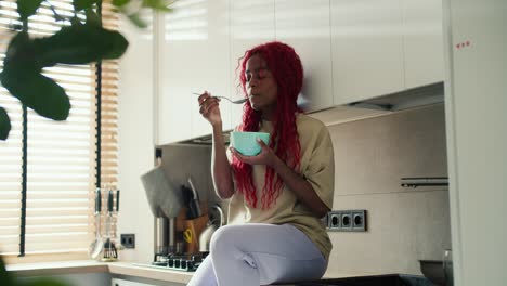 red headed woman enjoying her breakfast in the kitchen, eating cereals from the bowl