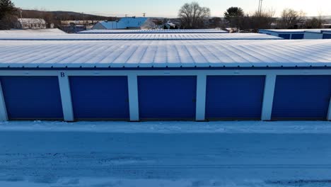 aerial trucking shot of rental garage units with blue doors at snowy winter day