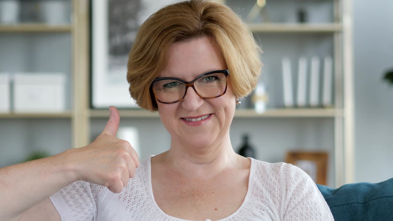 pulgares hacia arriba por la mujer mayor vieja en el trabajo, mirando a la cámara