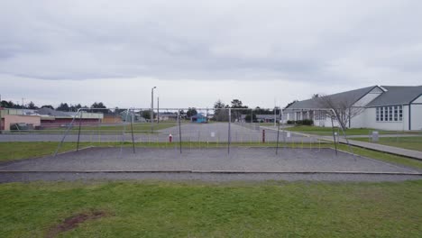 Aerial reverse dolly of empty swing set on green grass as seagull flies